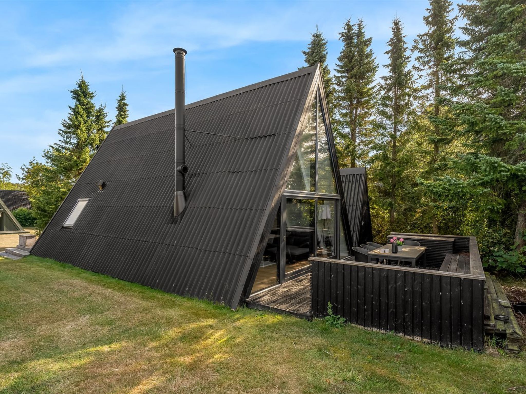 Una casa moderna con techo inclinado, una chimenea y un ventanal de vidrio que da a una terraza al aire libre.