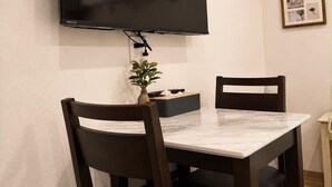 Un comedor con un televisor de pantalla plana montado en la pared, una mesa de mármol y dos sillas de madera oscura.