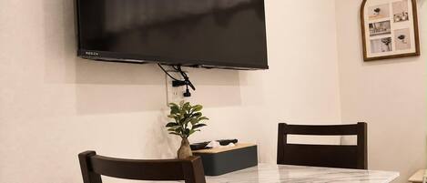 Un comedor con un televisor de pantalla plana montado en la pared, una mesa de mármol y dos sillas de madera oscura.