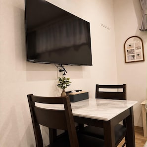 Un comedor con un televisor de pantalla plana montado en la pared, una mesa de mármol y dos sillas de madera oscura.