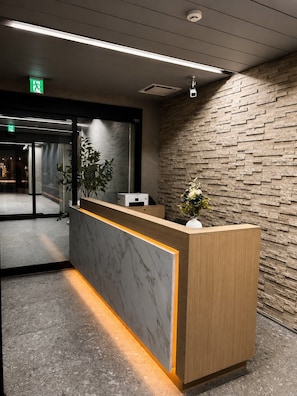 Una recepción con un panel de mármol, una planta en maceta y una pared con textura.