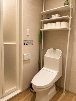 Un baño con inodoro, estante con papel higiénico y escoba.