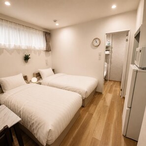 Habitación de hotel con dos camas, una mesita de noche con lámpara, un reloj en la pared y un refrigerador.