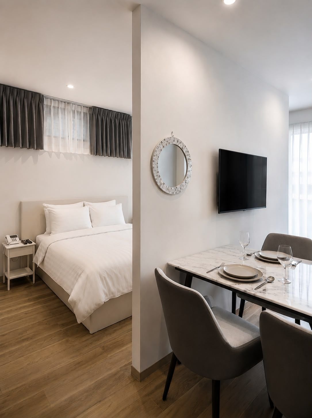 A hotel room with a bed, bedside table, nightstand, and a dining area with a table, chairs, and a flat-screen TV.