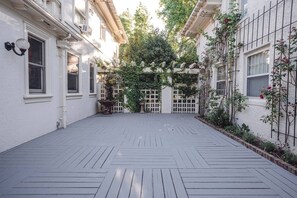 A courtyard with a wooden deck, white walls, and a white fence.