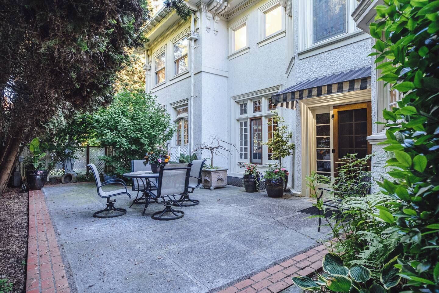 A courtyard with a patio table and chairs, surrounded by potted plants and a building with a door.