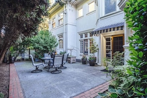 A courtyard with a patio table and chairs, surrounded by potted plants and a building with a door.