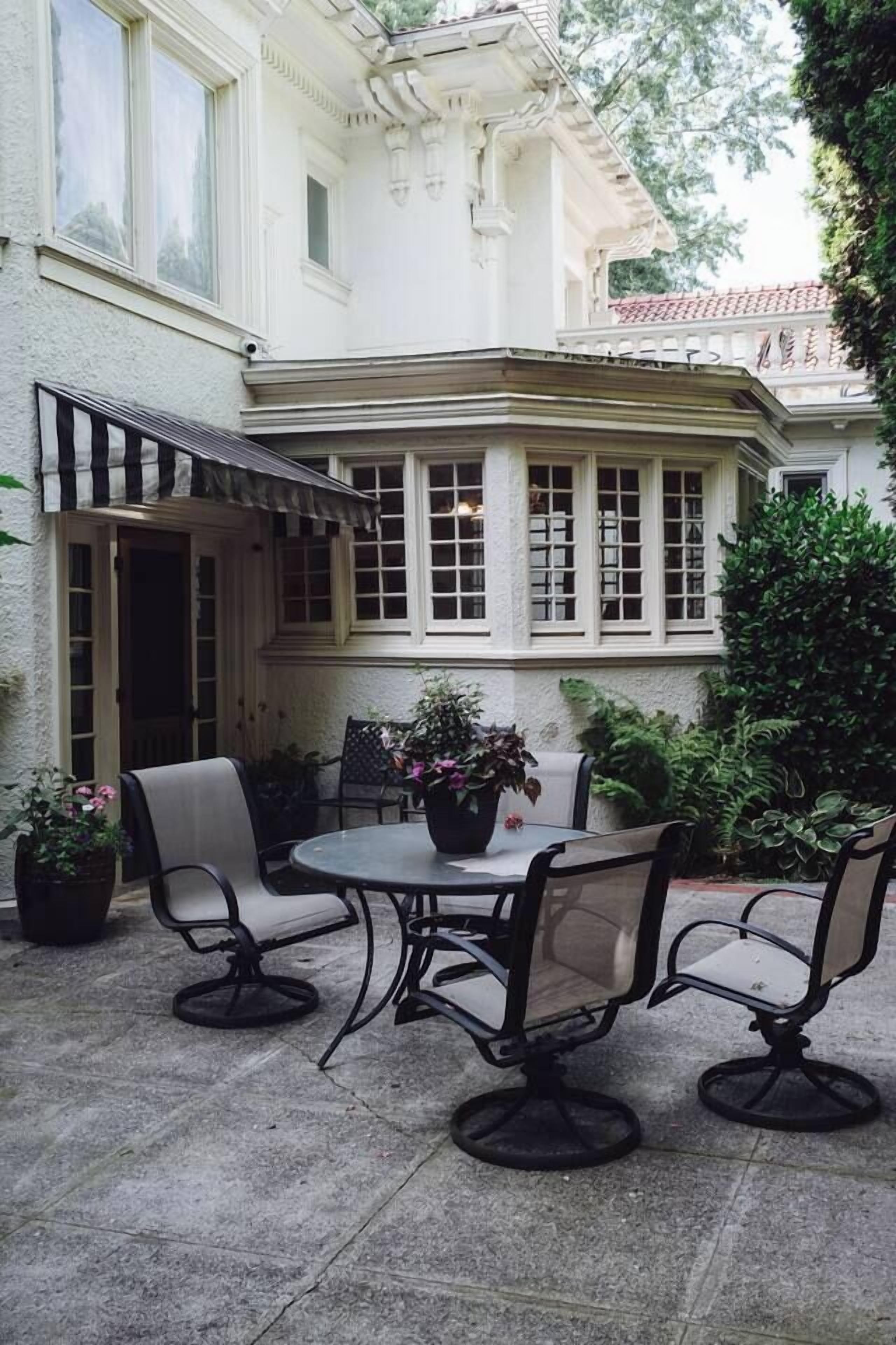 A patio with a table and four chairs, surrounded by potted plants and a white building with large windows.