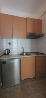 Cocina compacta con armarios de madera, un refrigerador de acero inoxidable, un lavamanos y una estufa.
