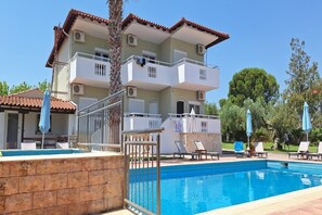 Un edificio de dos pisos con piscina, balcones y mobiliario de exterior.