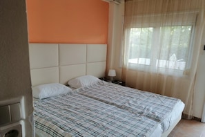 A bedroom with a bed, a nightstand, a window with curtains, and a wall with a color accent. - Villa Ilios Pefkohori (Kassandra)