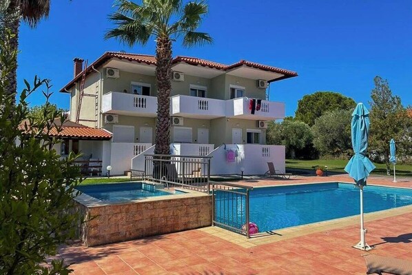 A two-story building with a swimming pool, balconies, and a palm tree. - Villa Ilios Pefkohori (Kassandra)