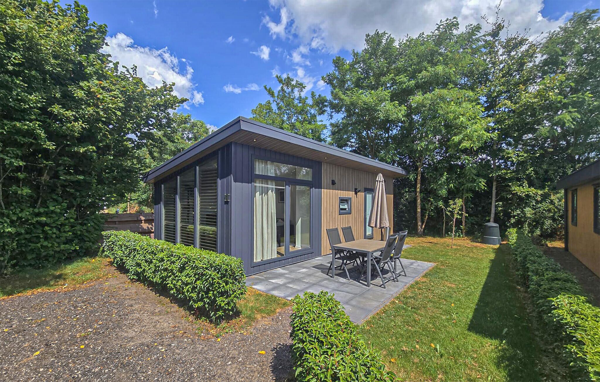 Une terrasse extérieure moderne, dotée d’une table et de chaises, et entourée de haies et d’arbres bien entretenus.