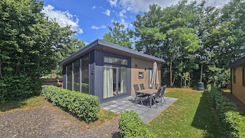 Une terrasse extérieure moderne, dotée d’une table et de chaises, et entourée de haies et d’arbres bien entretenus.