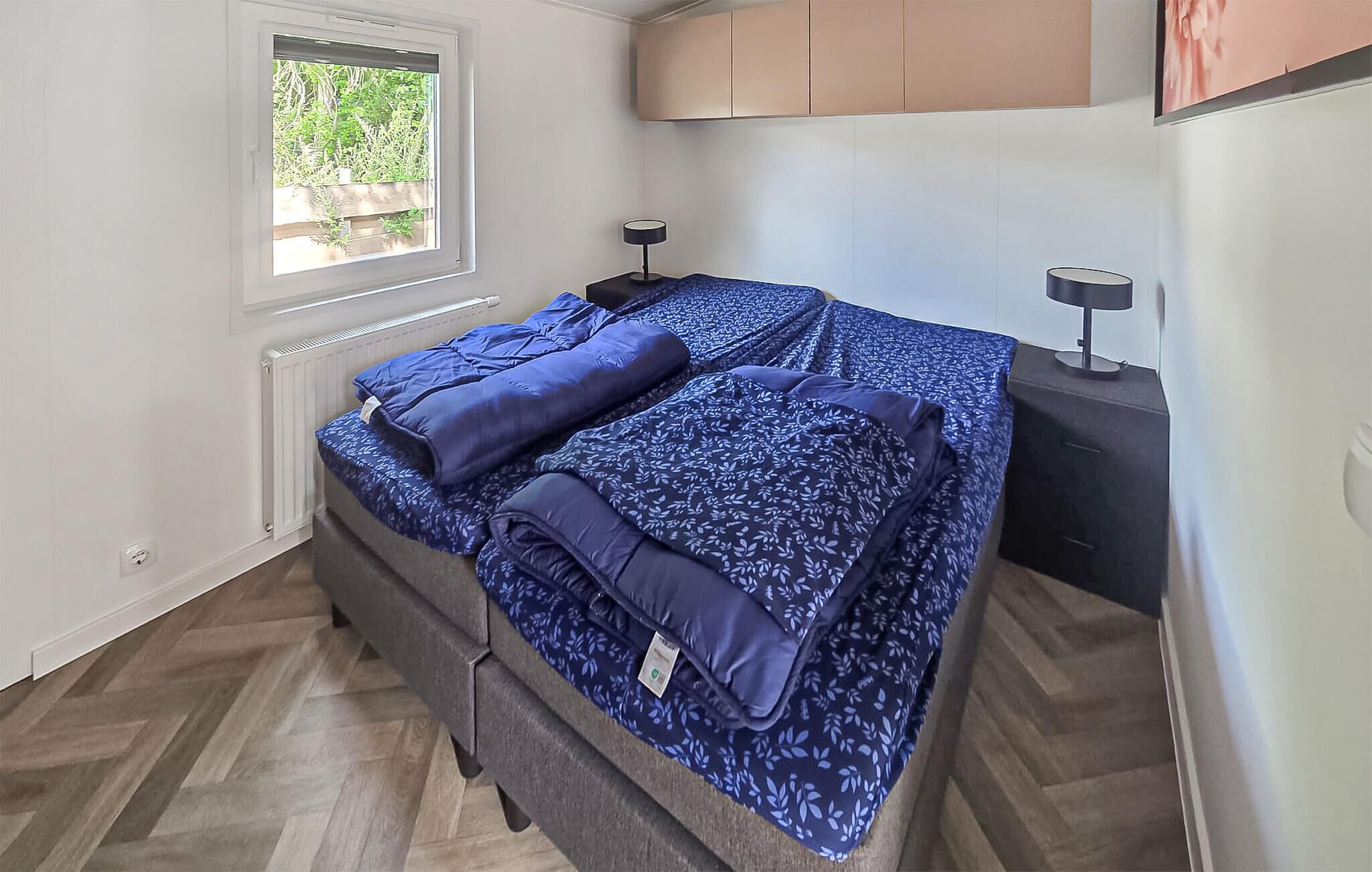 Une chambre à coucher avec un lit, deux tables de chevet, une fenêtre et un radiateur.