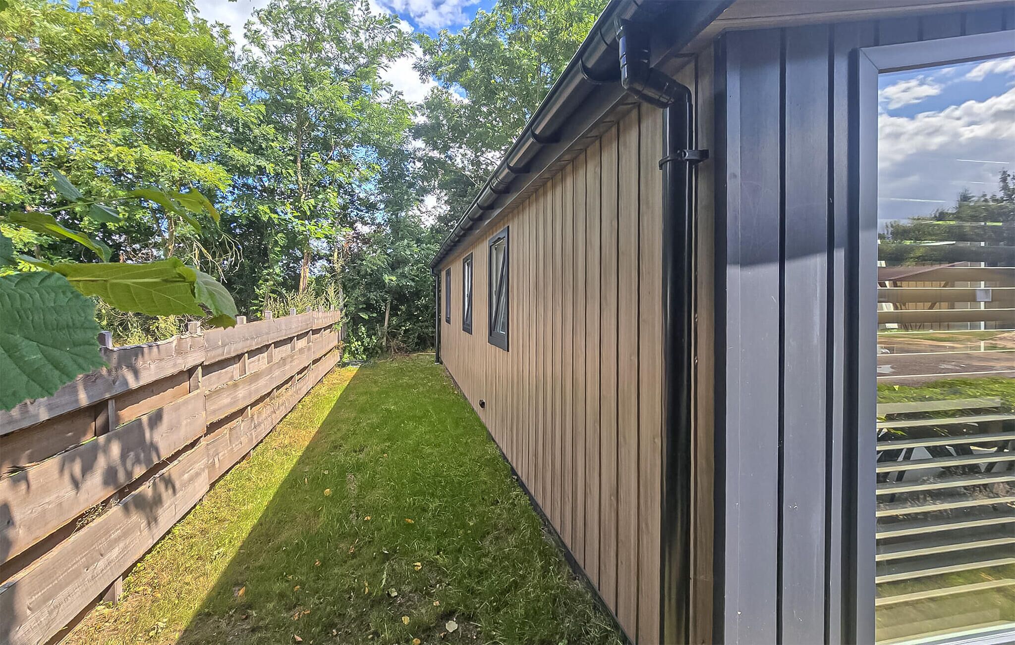 Un petit jardin clos de murs, avec une terrasse en bois et un bâtiment doté de grandes fenêtres.