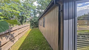 Un petit jardin clos de murs, avec une terrasse en bois et un bâtiment doté de grandes fenêtres.