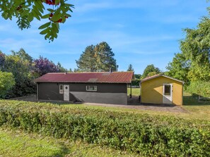 Ein zweistöckiges Gebäude mit rotem Dach, einem kleinen angebauten Schuppen und einer gepflegten Hecke im Vordergrund.