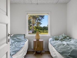 Ein Schlafzimmer mit zwei Einzelbetten, einem Fenster mit Blick auf Bäume und einem Nachttisch mit Lampe.