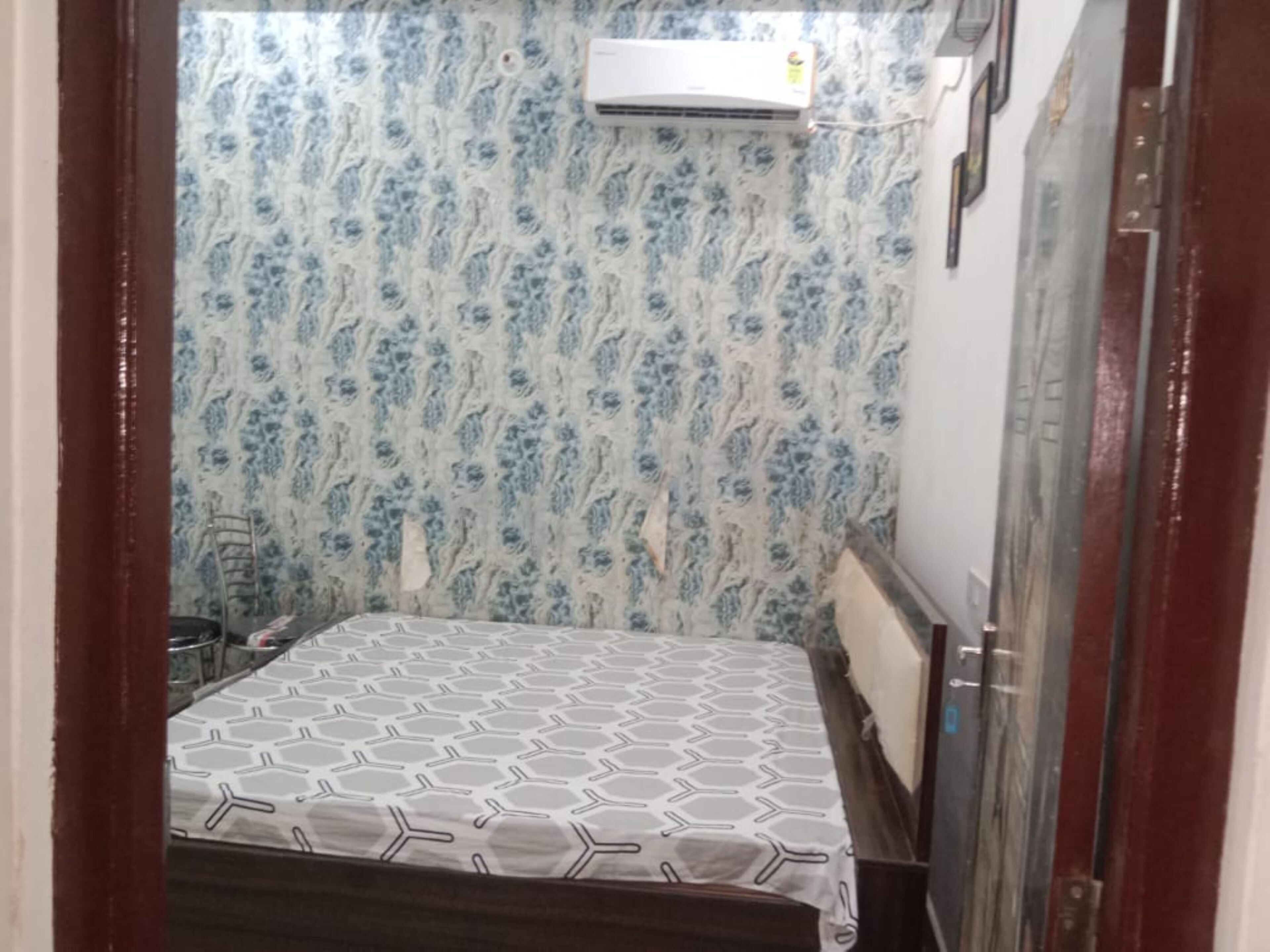 Una habitación pequeña con una cama, una silla y un equipo de aire acondicionado en la pared.