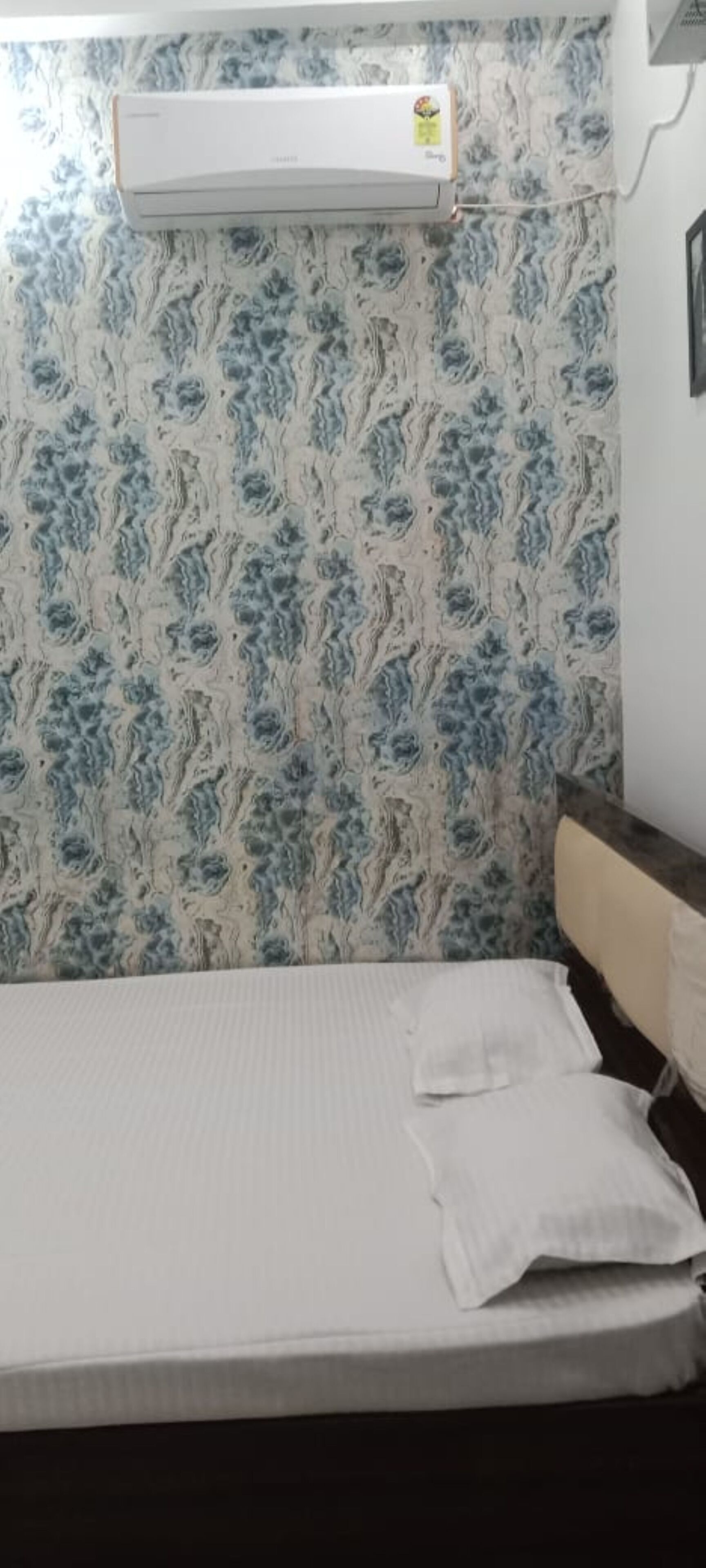 Una habitación con una cama, aire acondicionado de pared y papel tapiz estampado.