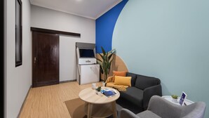 A modern living room with a sofa, a small table, and a kitchen area with a refrigerator.