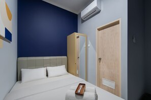 A hotel room with a bed, a wooden wardrobe, a door, and an air conditioning unit.