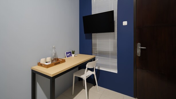 A small room with a desk, chair, a television mounted on the wall, and a door.