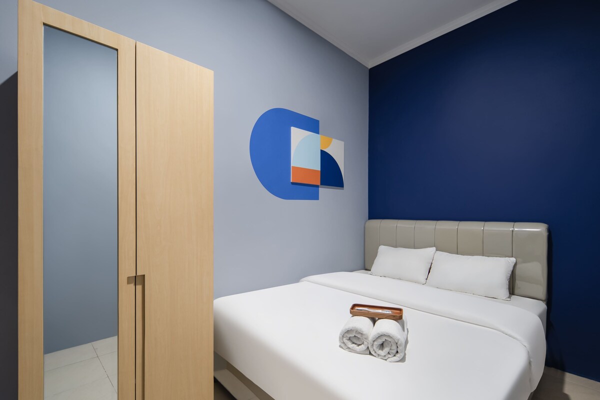 A hotel room with a bed, a wooden wardrobe, a blue accent wall, and a logo on the wall.