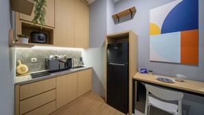 A compact kitchen with wooden cabinets, a built-in oven, a black refrigerator, and a small dining area with a white chair.