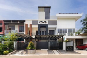 Un edificio moderno con un llamativo letrero 'Cove', una entrada con portón y un coche rojo estacionado al frente.