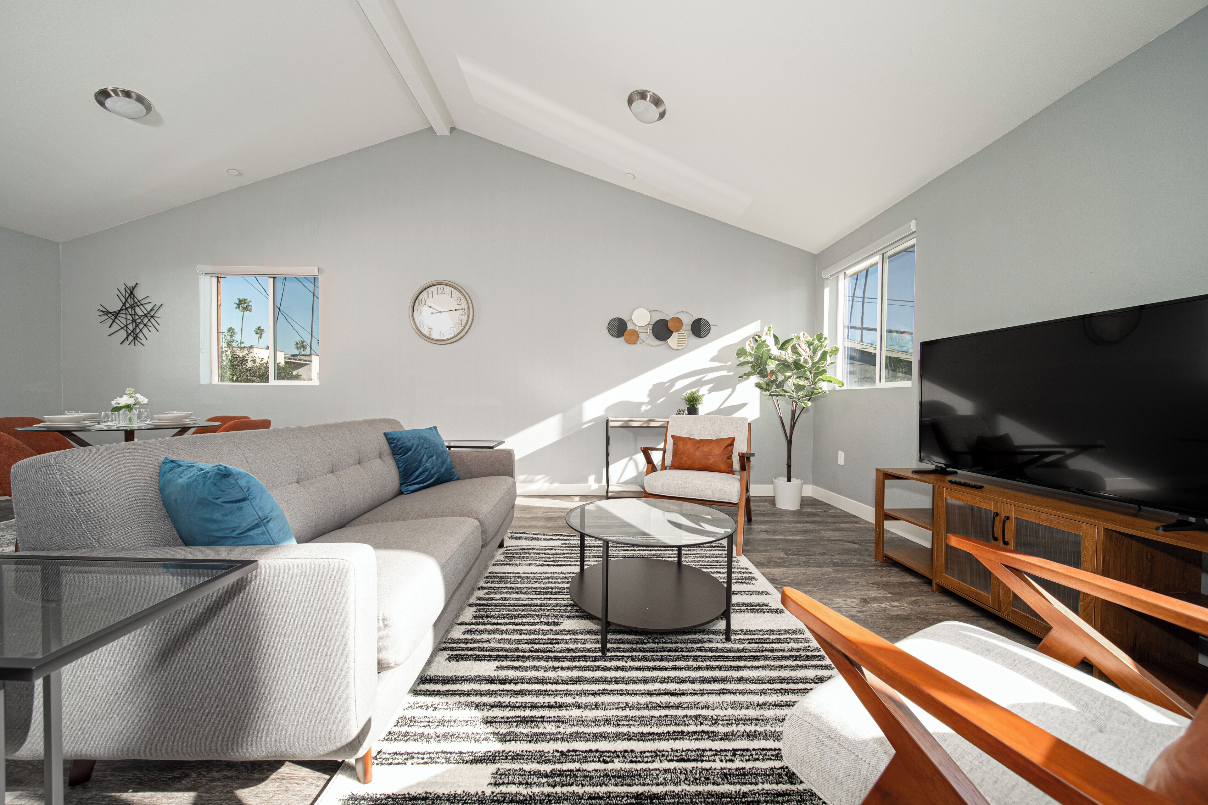 A modern living room with a grey sofa, a coffee table, a TV, and a large window providing natural light.