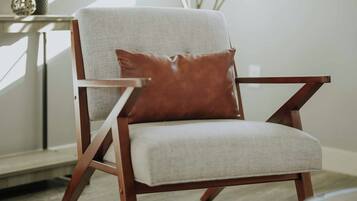 A modern armchair with a cushion and a brown accent pillow, positioned in a room with a large window, a plant, and a patterned rug.
