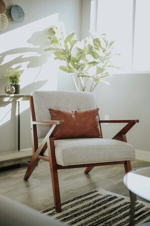A modern armchair with a cushion and a brown accent pillow, positioned in a room with a large window, a plant, and a patterned rug. - Stylish 3BR LA Home Near Beverly Hills, LACMA & The Grove (Los Angeles)