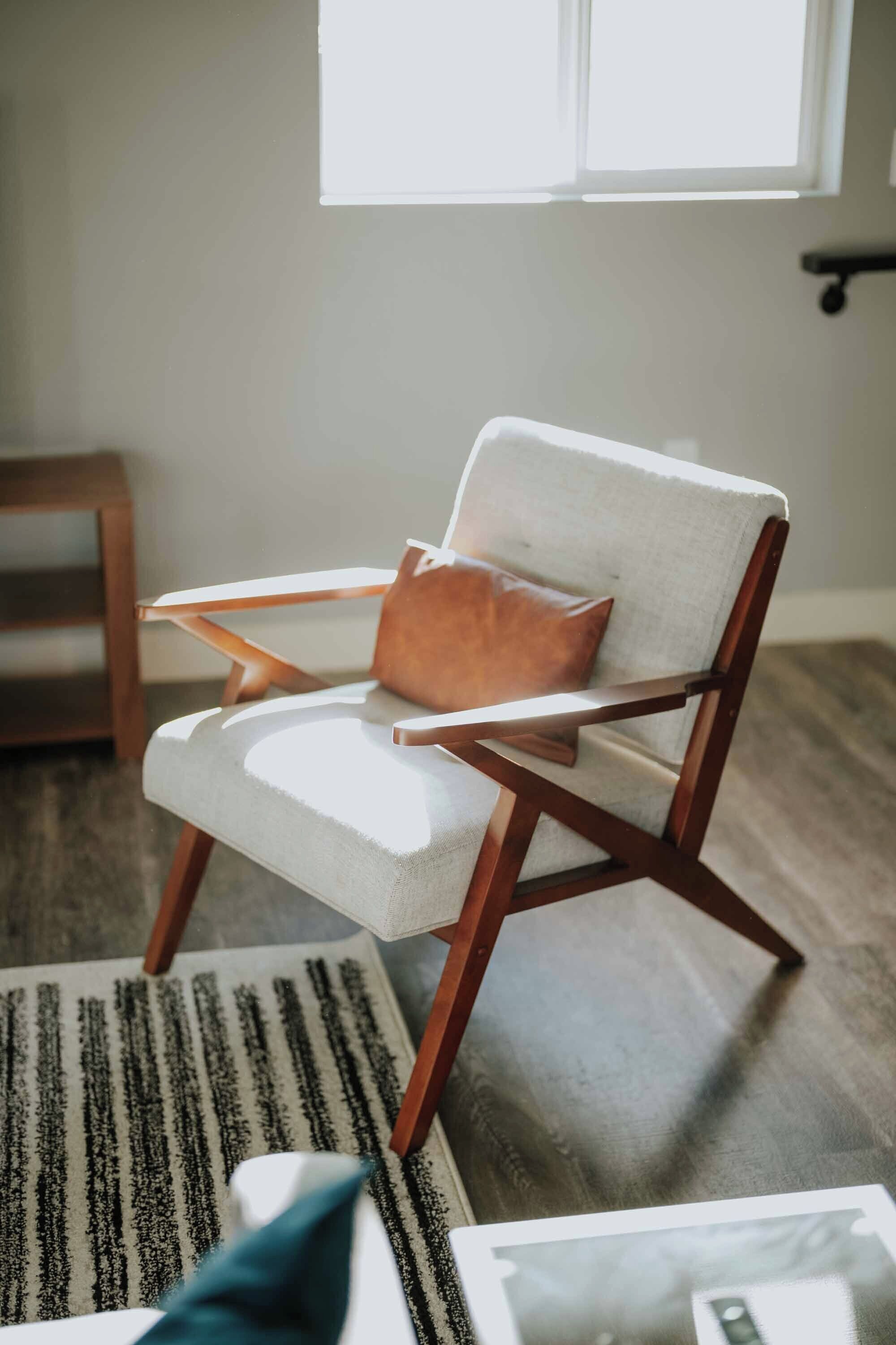 A modern armchair with a cushion and a wooden frame, placed on a patterned rug in a room with hardwood flooring.