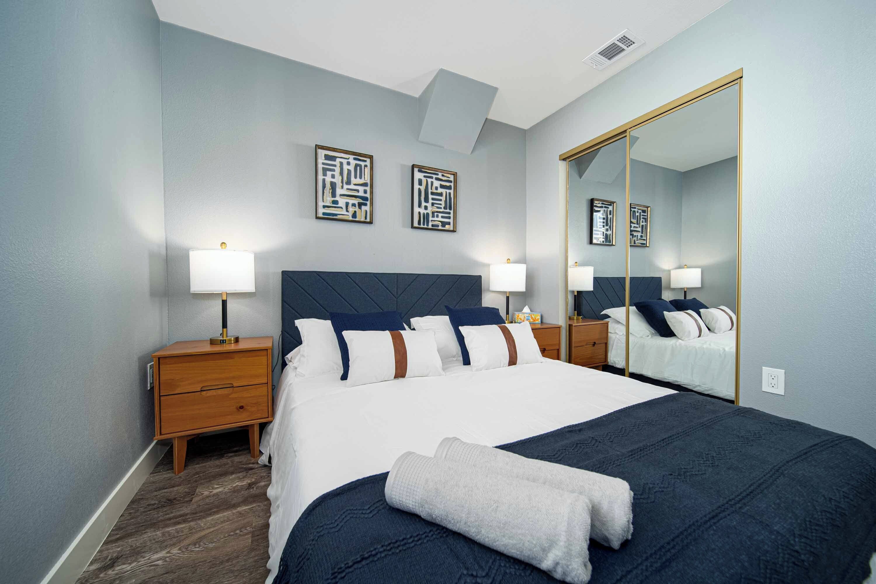 Habitación de hotel con una cama grande, dos mesitas de noche, un espejo y obras de arte en la pared.