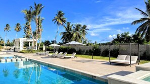 A swimming pool with lounge chairs and umbrellas, surrounded by palm trees and a clear sky. - Peaceful Pool View Walk to Fun Beach Dine Shop (Punta Cana)