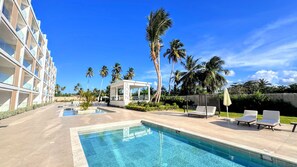 A hotel pool area with a clear blue pool, lounge chairs, and palm trees. - Peaceful Pool View Walk to Fun Beach Dine Shop (Punta Cana)