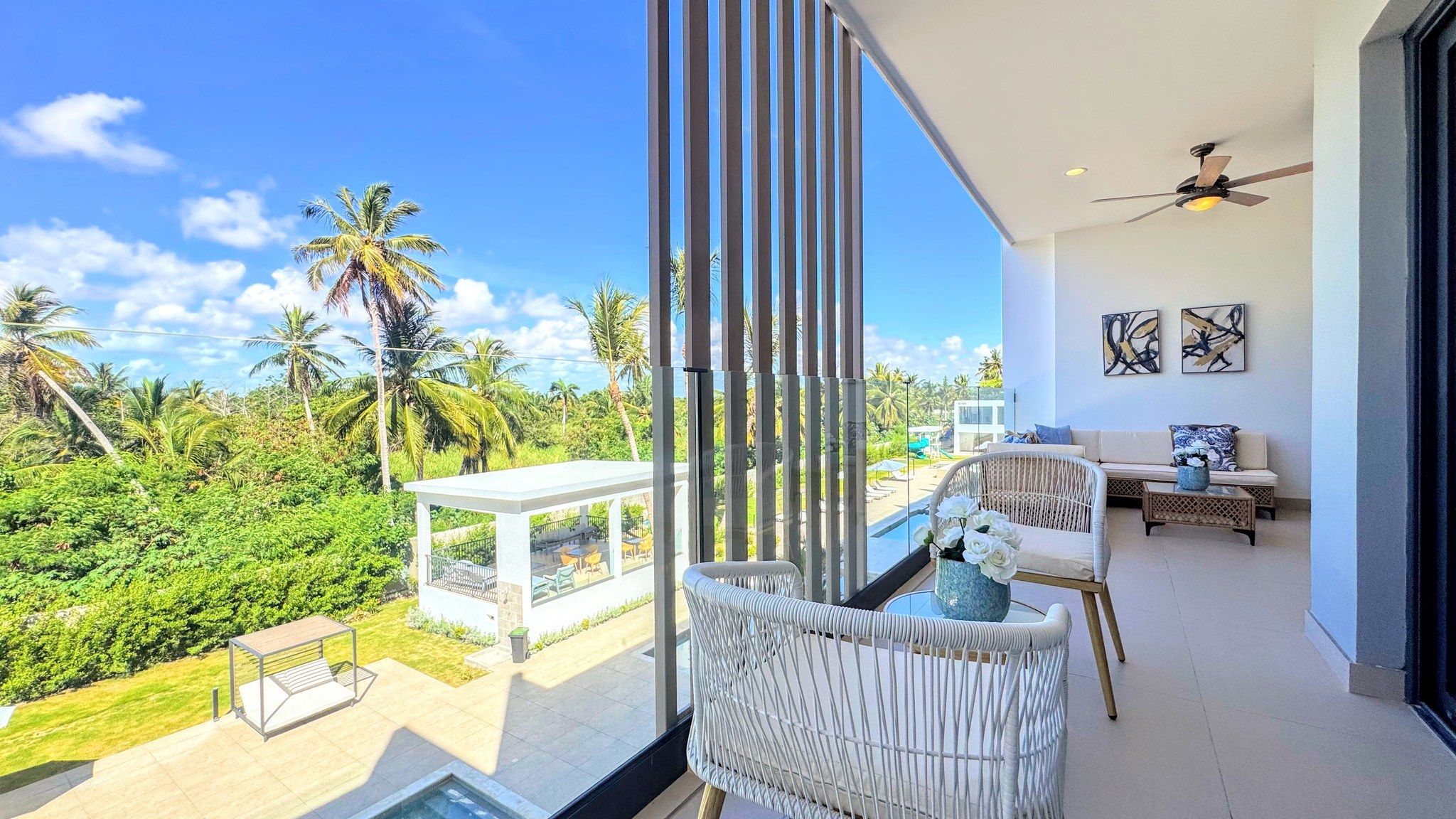 Ein moderner Balkon mit Blick auf eine tropische Landschaft, darunter Palmen und ein Schwimmbad.