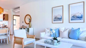 A modern living room with a white sofa, a coffee table, and a dining area with a white table and chairs. - Peaceful Pool View Walk to Fun Beach Dine Shop (Punta Cana)