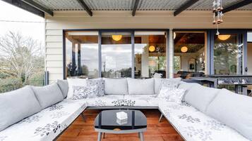 A modern outdoor seating area with a sectional sofa and a small table, large windows, and a metal roof structure.
