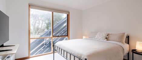 A bedroom with a bed, a desk, and a large window.