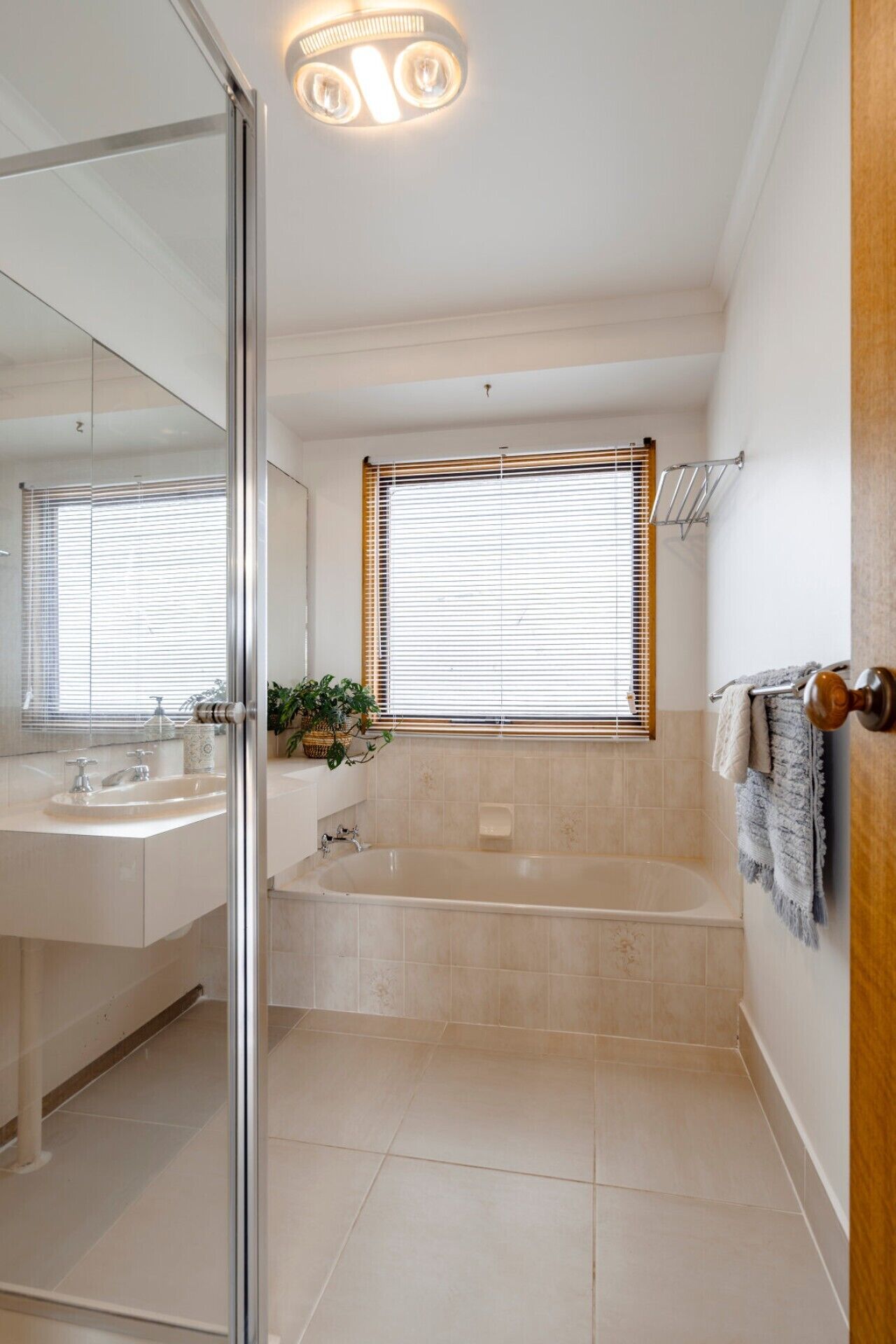 A modern bathroom with a glass shower enclosure, a bathtub, a vanity with a sink, and a window with blinds.