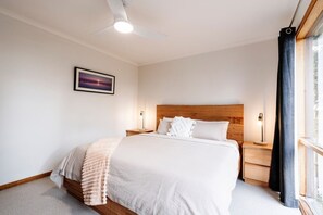 A bedroom with a bed, bedside tables, a ceiling fan, a window with curtains, and a framed picture on the wall.