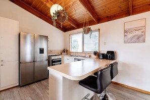 A modern kitchen with a stainless steel refrigerator, a gas stove, and a wooden ceiling.