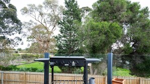 Un espace barbecue extérieur avec une table et une bouteille de gaz, installé sur une terrasse en bois.