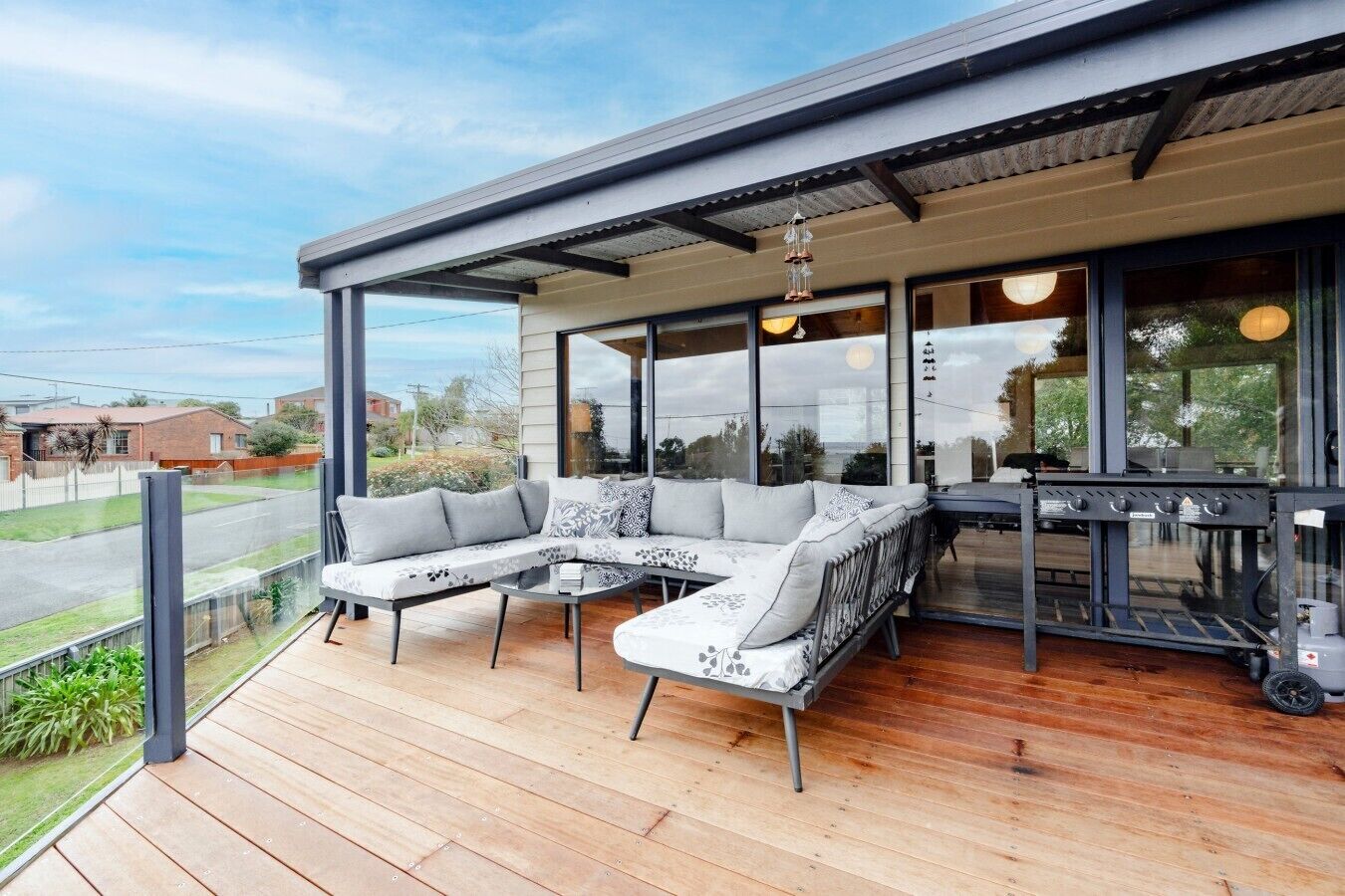 A modern outdoor seating area with a wooden deck, a sectional sofa, and a barbecue grill.