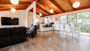 Un vaste espace de vie doté d’un plafond en bois, d’un téléviseur à écran plat, d’un canapé et d’un coin repas avec des chaises et une table.