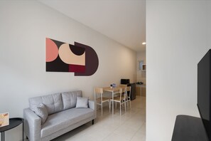 A modern living room with a grey sofa, a dining table with chairs, and a kitchen area in the background.