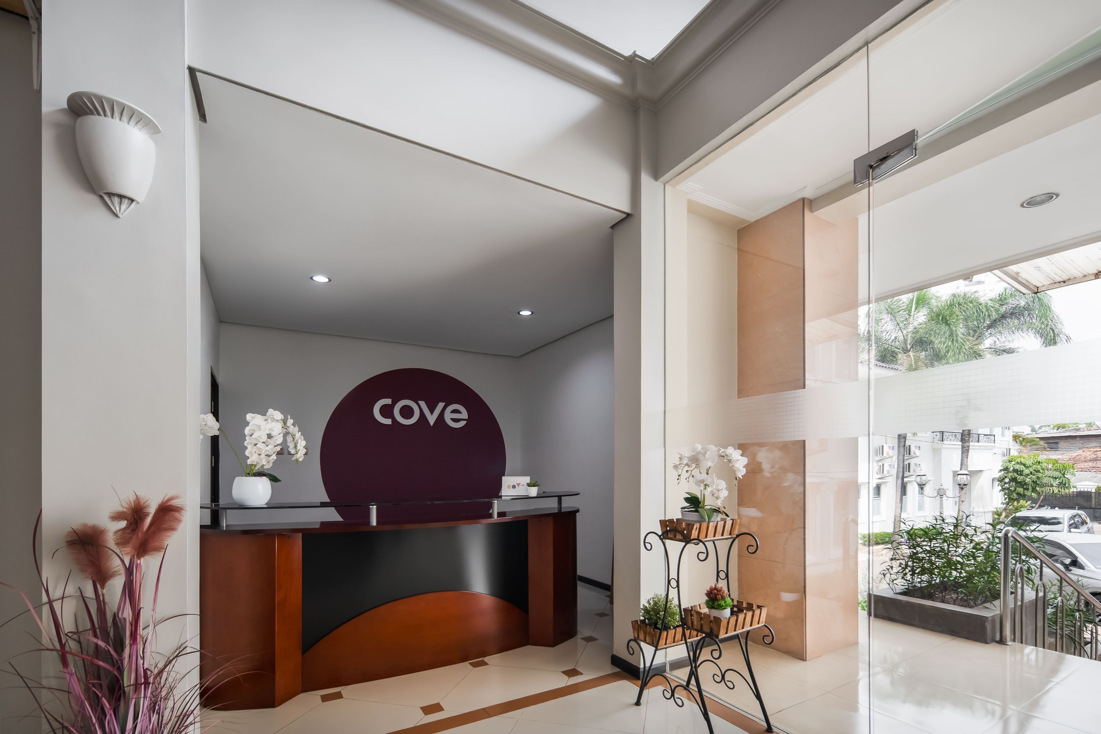 A reception desk with a 'cove' sign, a glass door leading outside, and a potted plant with white flowers.